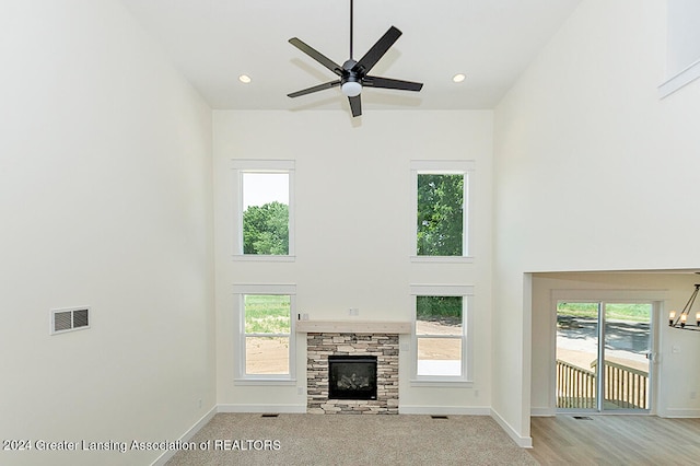 unfurnished living room with ceiling fan with notable chandelier, plenty of natural light, a towering ceiling, and a stone fireplace