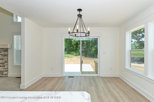 unfurnished dining area with light wood-type flooring, a notable chandelier, and a healthy amount of sunlight