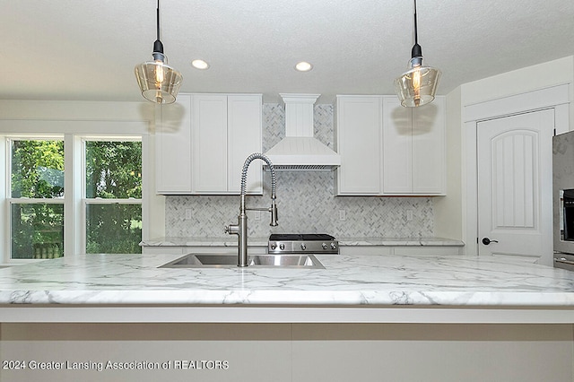 kitchen with a center island with sink, pendant lighting, white cabinets, and custom range hood