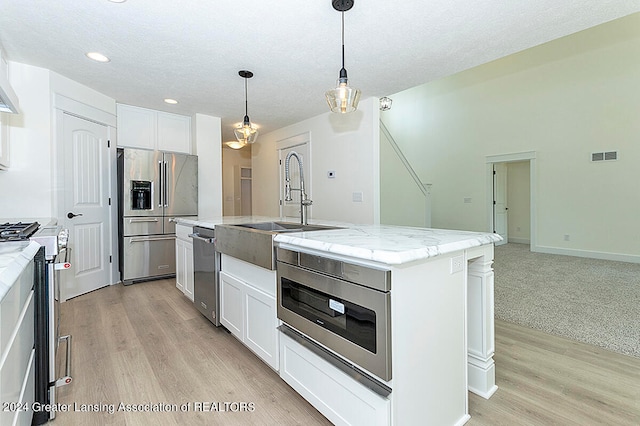 kitchen with appliances with stainless steel finishes, decorative light fixtures, white cabinetry, light stone counters, and a center island with sink