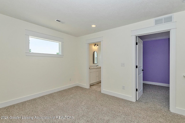 unfurnished bedroom with ensuite bathroom, light colored carpet, and a textured ceiling