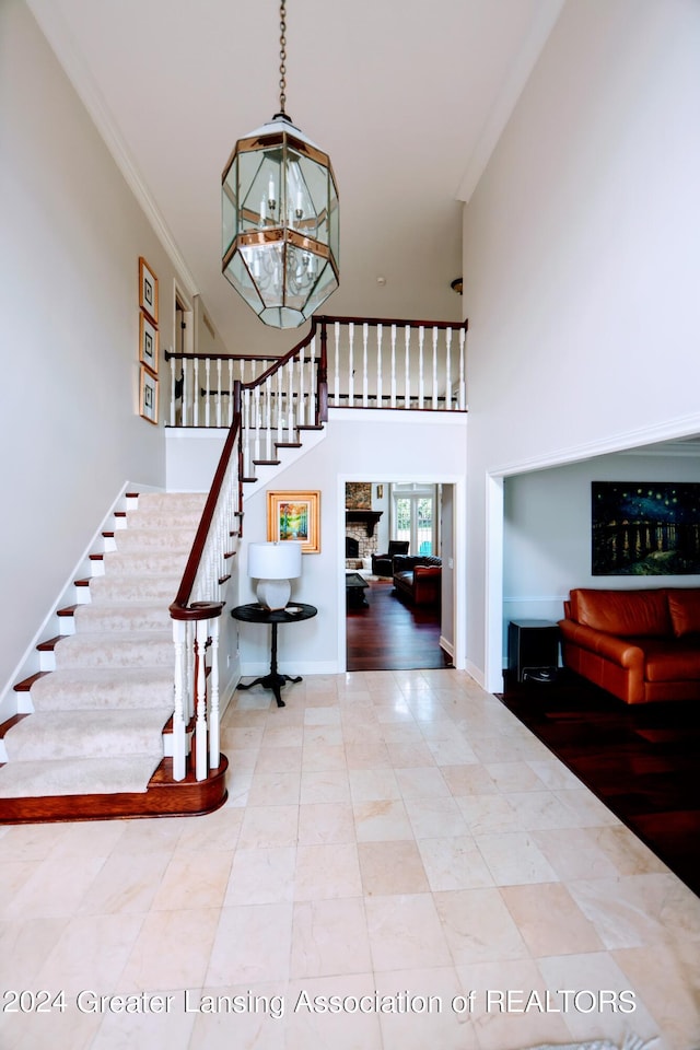 stairs featuring hardwood / wood-style floors, an inviting chandelier, ornamental molding, and a stone fireplace