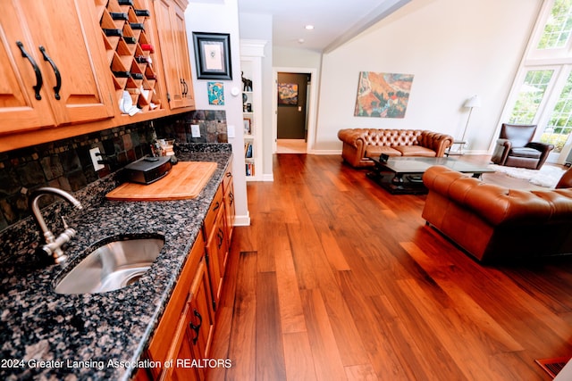 kitchen with sink, tasteful backsplash, dark stone counters, lofted ceiling, and hardwood / wood-style flooring