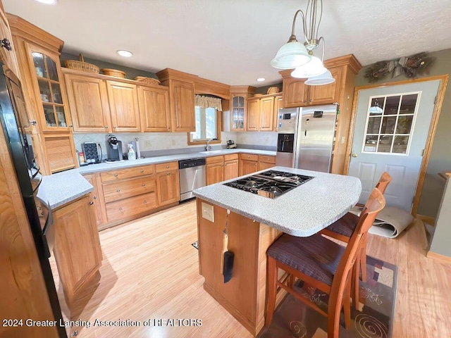 kitchen featuring appliances with stainless steel finishes, a center island, hanging light fixtures, and light wood-type flooring