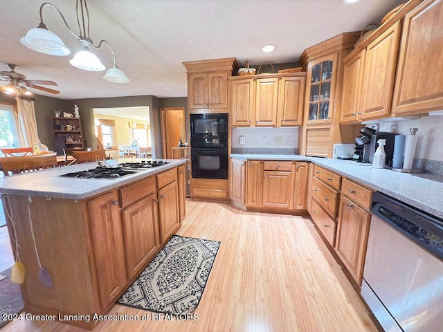 kitchen featuring a kitchen island, hanging light fixtures, ceiling fan, stainless steel appliances, and light hardwood / wood-style flooring