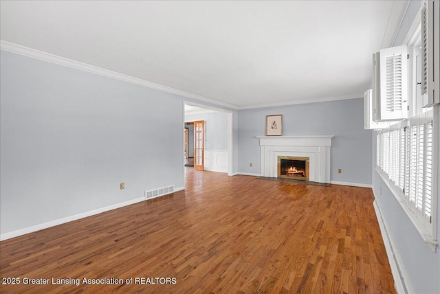 unfurnished living room featuring wood finished floors, a fireplace with flush hearth, baseboards, visible vents, and crown molding