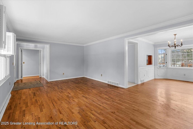 unfurnished living room featuring visible vents, a wainscoted wall, ornamental molding, wood finished floors, and an inviting chandelier