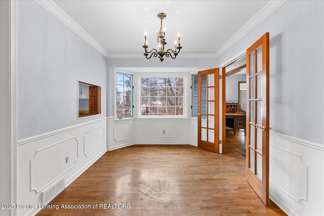 unfurnished dining area featuring wood finished floors, french doors, visible vents, and an inviting chandelier