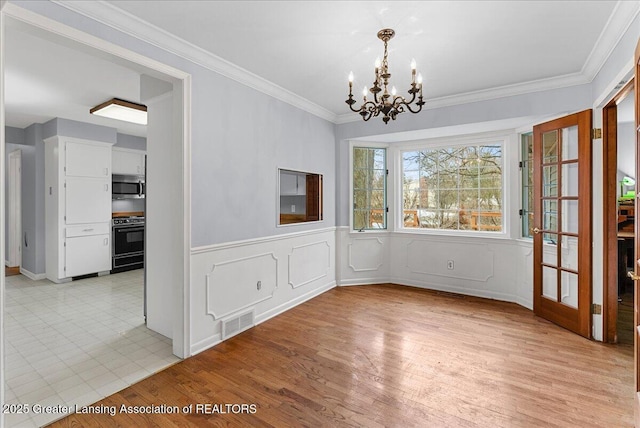 unfurnished dining area featuring visible vents, wainscoting, crown molding, light wood-type flooring, and a notable chandelier