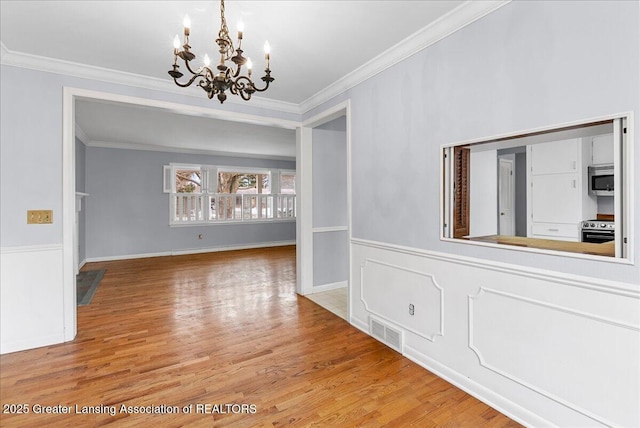 unfurnished dining area featuring a wainscoted wall, visible vents, crown molding, and wood finished floors