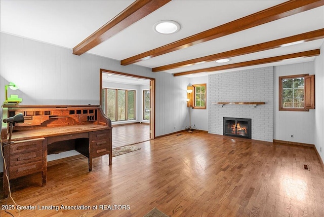 living room with visible vents, a brick fireplace, wood finished floors, beamed ceiling, and baseboards