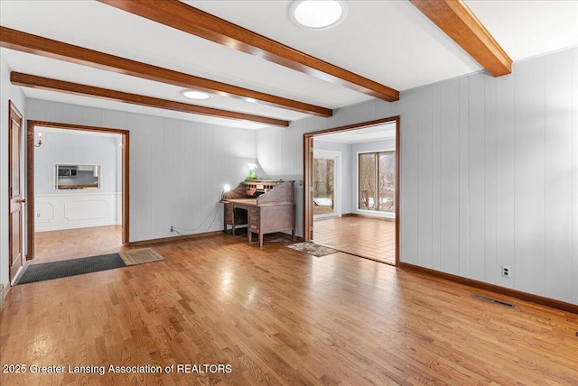 unfurnished living room with light wood-style flooring, beamed ceiling, visible vents, and baseboards