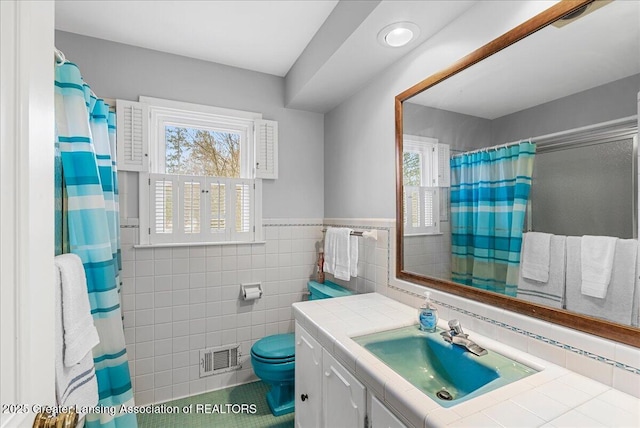 full bathroom with tile walls, visible vents, a shower with shower curtain, toilet, and vanity