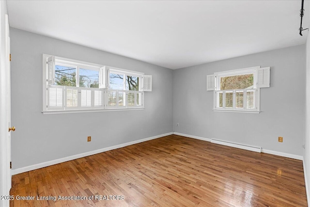 empty room with baseboards, baseboard heating, a wealth of natural light, and wood finished floors