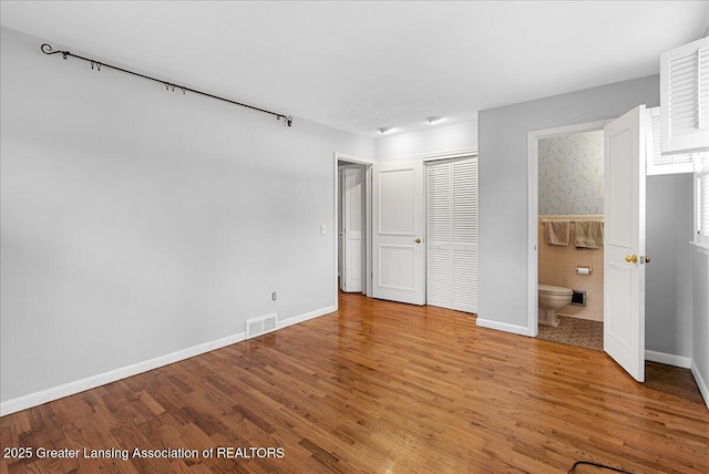 unfurnished bedroom with light wood-style floors, a closet, tile walls, and ensuite bathroom