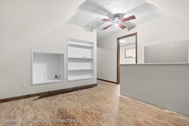 empty room featuring a textured ceiling, ceiling fan, light hardwood / wood-style floors, vaulted ceiling, and built in shelves