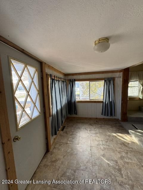 empty room featuring wooden walls, a textured ceiling, and a healthy amount of sunlight