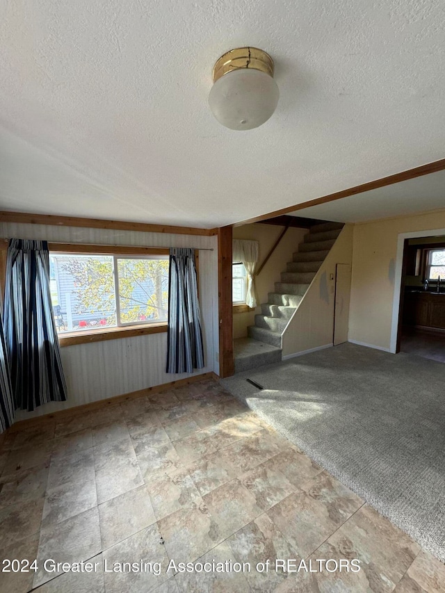 carpeted spare room with a textured ceiling and wooden walls