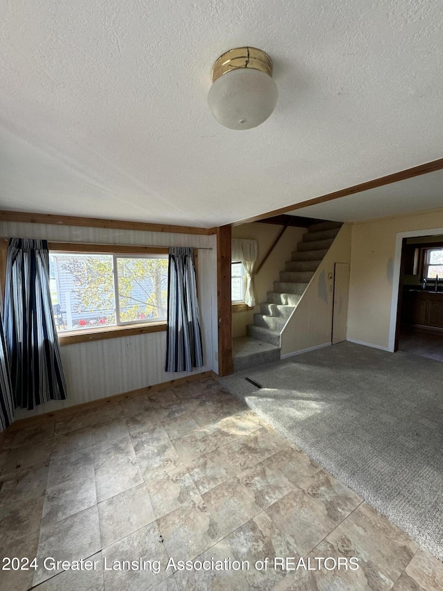 unfurnished living room with baseboards, a textured ceiling, stairway, and stone finish flooring