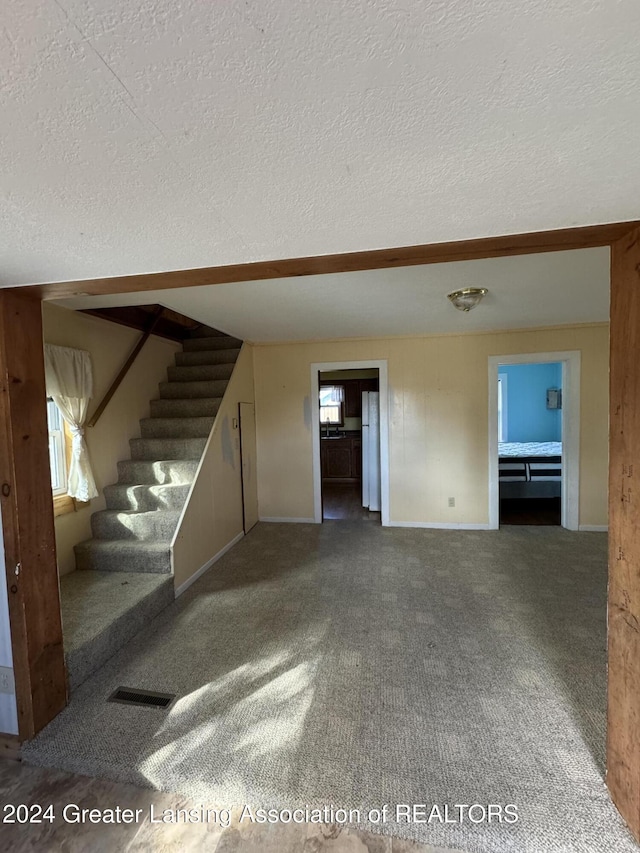 unfurnished living room with stairs, carpet floors, baseboards, visible vents, and a textured ceiling