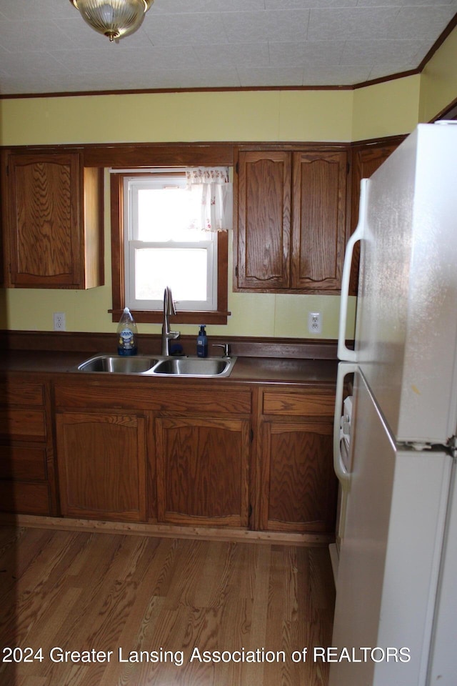 kitchen with a sink, dark countertops, light wood-style floors, freestanding refrigerator, and brown cabinetry