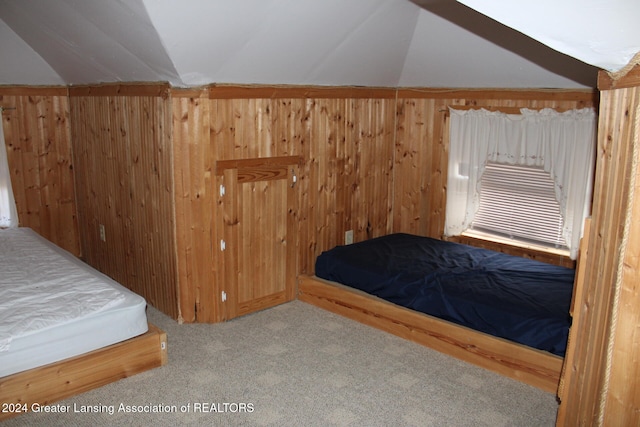 carpeted bedroom with lofted ceiling and wood walls