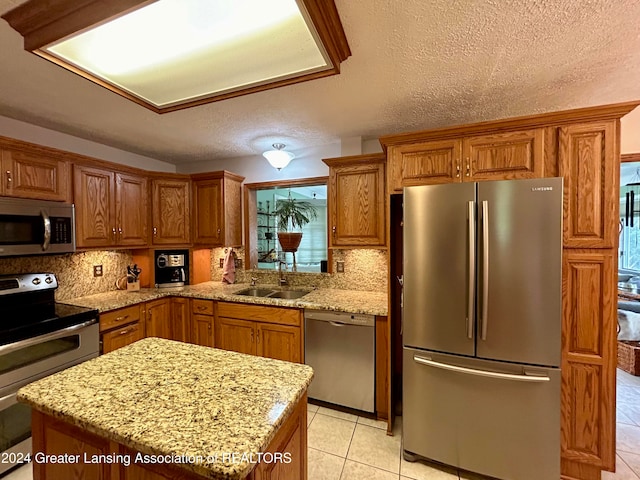 kitchen featuring light stone countertops, sink, appliances with stainless steel finishes, a kitchen island, and a textured ceiling