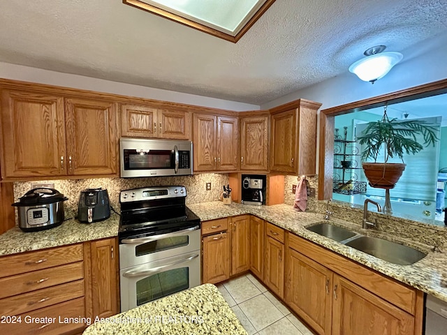 kitchen with light tile patterned floors, appliances with stainless steel finishes, a textured ceiling, light stone countertops, and sink