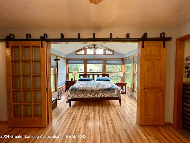 bedroom featuring light hardwood / wood-style flooring, lofted ceiling, and a barn door