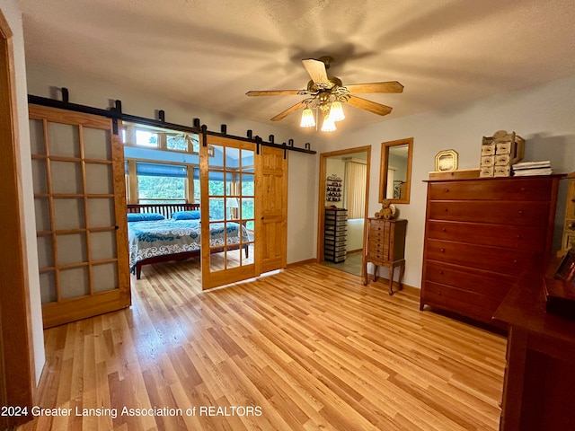 unfurnished bedroom featuring a barn door, a textured ceiling, light hardwood / wood-style floors, and ceiling fan