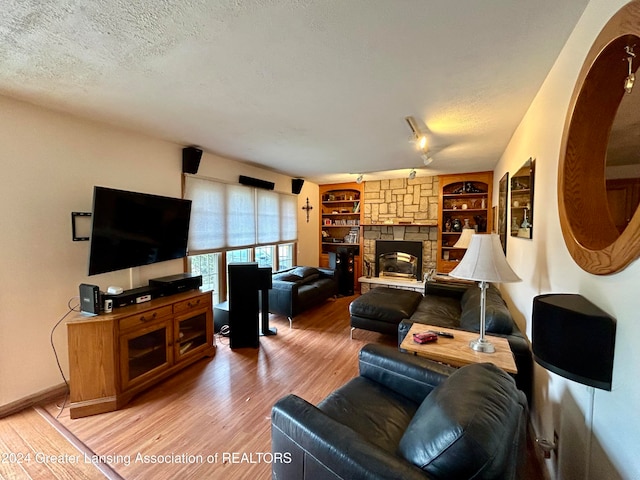 living room featuring built in features, wood-type flooring, a textured ceiling, and a fireplace