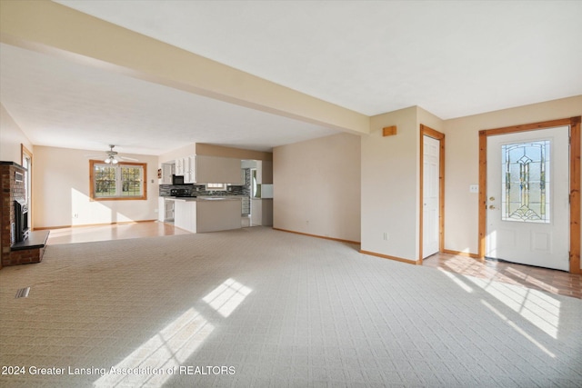 unfurnished living room featuring ceiling fan, a brick fireplace, and light colored carpet