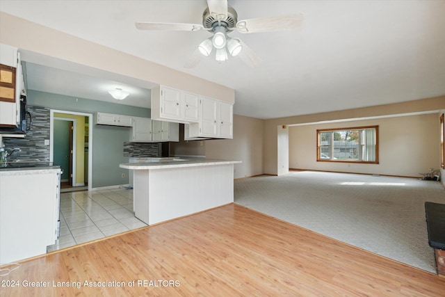 kitchen with kitchen peninsula, white cabinetry, tasteful backsplash, and light colored carpet