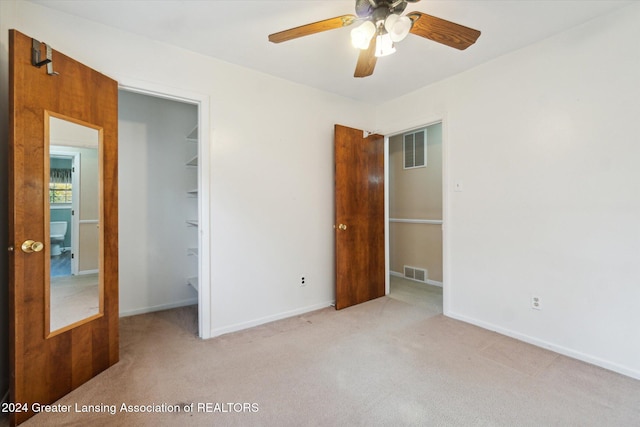 unfurnished bedroom with a walk in closet, light colored carpet, a closet, and ceiling fan