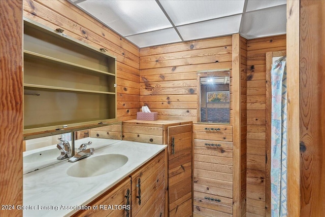 bathroom with vanity, wood walls, and a drop ceiling