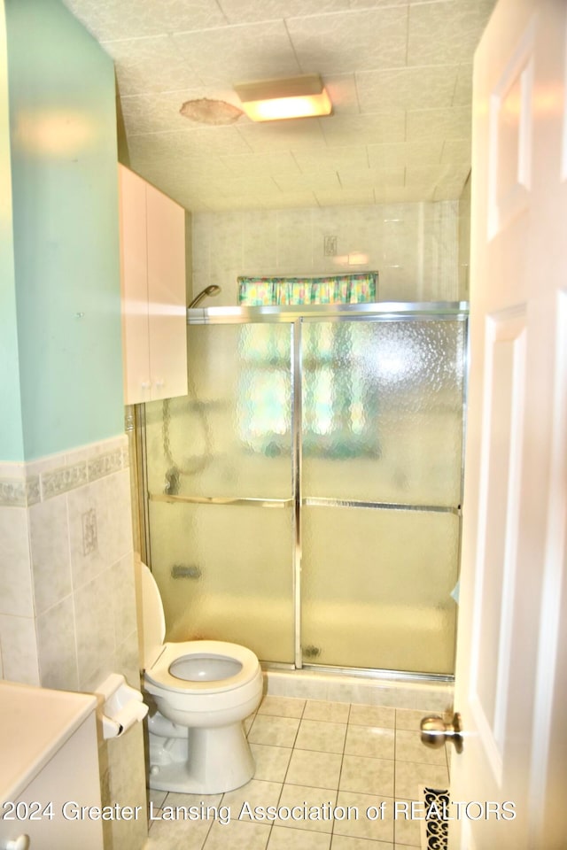 bathroom with tile walls, toilet, vanity, an enclosed shower, and tile patterned flooring