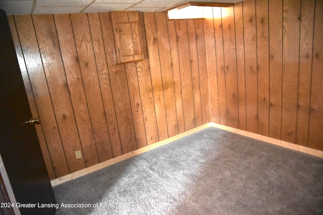 basement with a paneled ceiling, wooden walls, and carpet floors