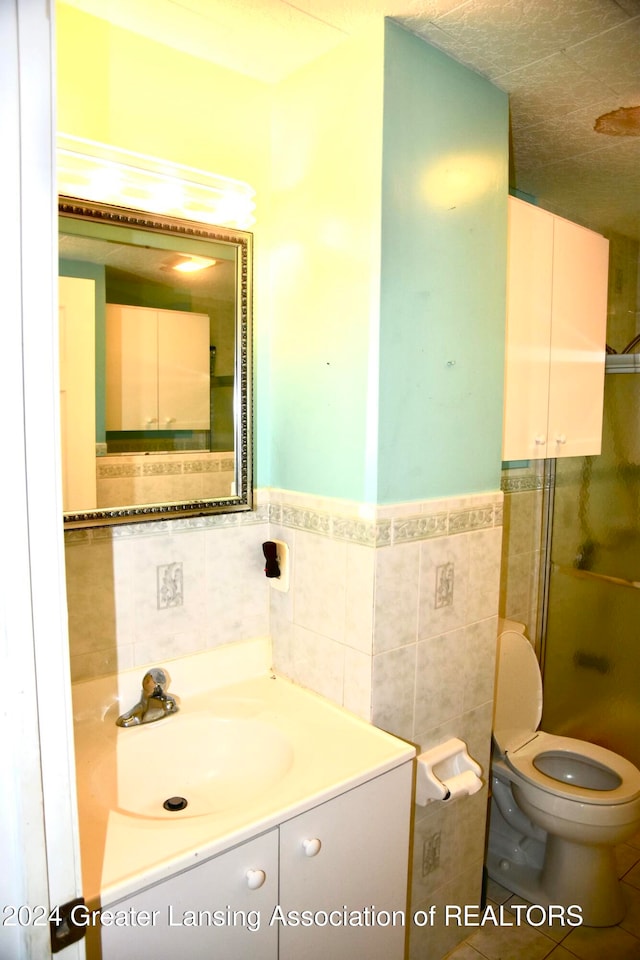 bathroom featuring vanity, toilet, tile walls, and a shower with shower door