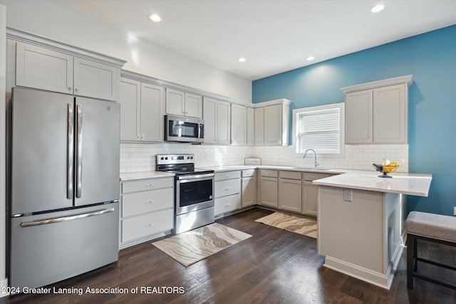 kitchen with appliances with stainless steel finishes, a kitchen bar, backsplash, light stone counters, and dark hardwood / wood-style floors