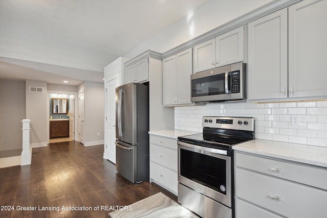 kitchen featuring decorative backsplash, dark hardwood / wood-style floors, gray cabinets, appliances with stainless steel finishes, and light stone counters