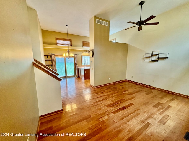 unfurnished living room featuring a towering ceiling, wood-type flooring, ceiling fan with notable chandelier, and sink