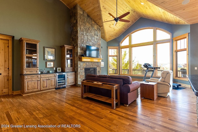 living room featuring wood ceiling, beverage cooler, high vaulted ceiling, dark wood-type flooring, and a stone fireplace