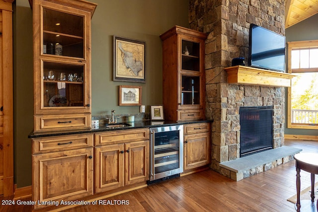 bar featuring sink, a stone fireplace, dark hardwood / wood-style flooring, lofted ceiling, and wine cooler