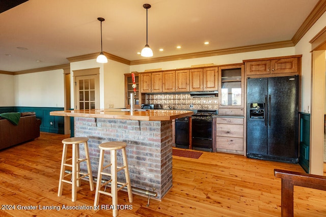 kitchen featuring black appliances, light wood-type flooring, a kitchen breakfast bar, crown molding, and a center island with sink