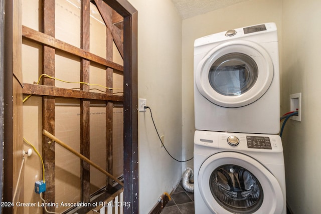 laundry room featuring stacked washer / dryer, a textured ceiling, and dark tile patterned flooring