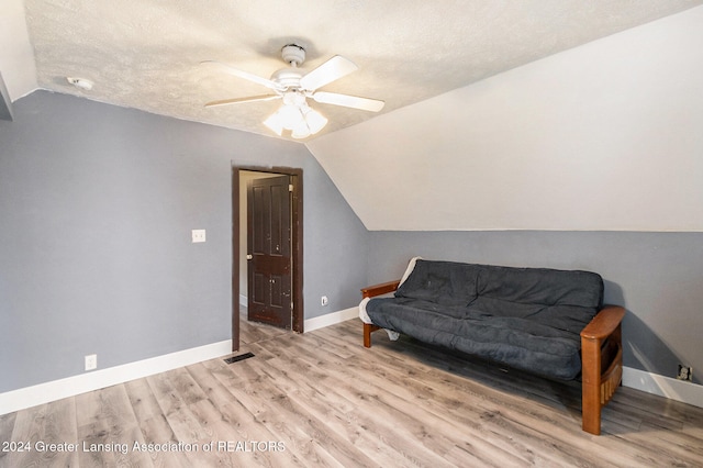 living area with vaulted ceiling, a textured ceiling, light wood-type flooring, and ceiling fan