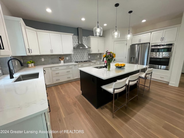 kitchen featuring an island with sink, wall chimney exhaust hood, sink, white cabinetry, and tasteful backsplash