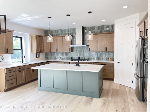 6119 Fresno Ln, East Lansing, MI 48823 - kitchen featuring wall chimney range hood, appliances with stainless steel finishes, a center island with sink, light countertops, and light wood-style flooring