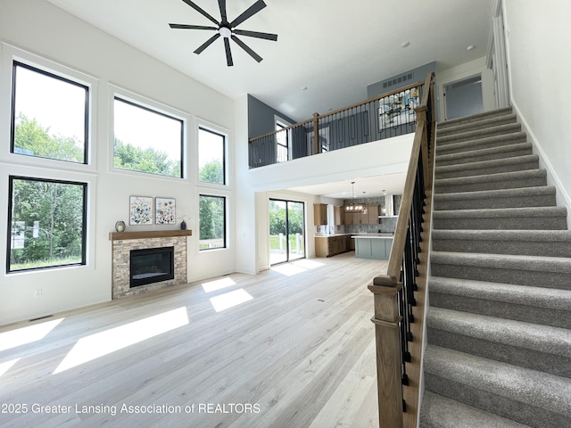6119 Fresno Ln, East Lansing, MI 48823 - unfurnished living room featuring a glass covered fireplace, a towering ceiling, stairs, light wood-style floors, and a ceiling fan
