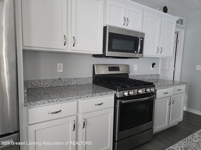 kitchen with white cabinets, a textured ceiling, light stone countertops, dark wood-type flooring, and stainless steel appliances